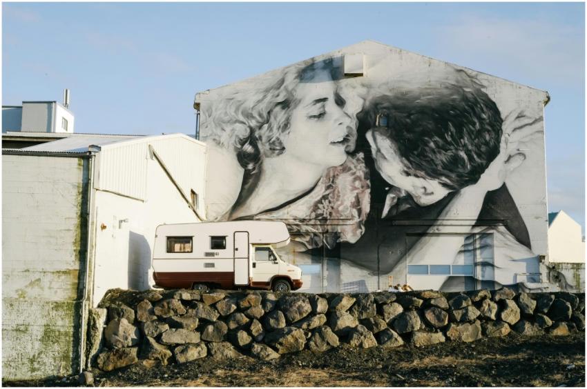 A campervan parked beside a large grayscale mural