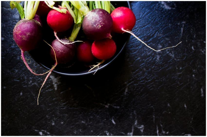 Vibrant red and purple radishes in a black bowl on