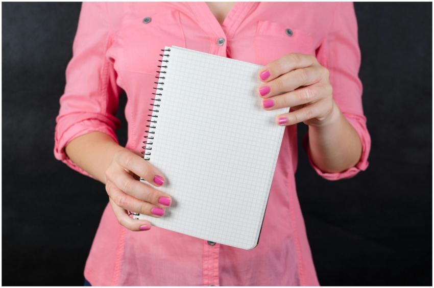 A woman in a pink shirt holds a blank notepad, ide