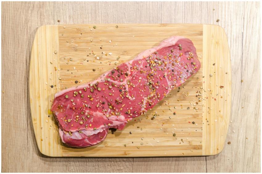 Raw beef steak seasoned with spices on a wooden ch