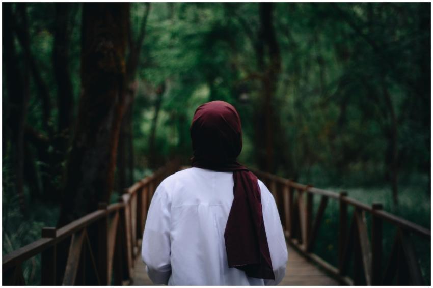 A woman in a hijab walks on a wooden bridge surrou