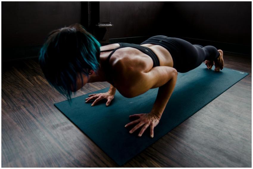 A fit woman with blue hair performs a push-up on a