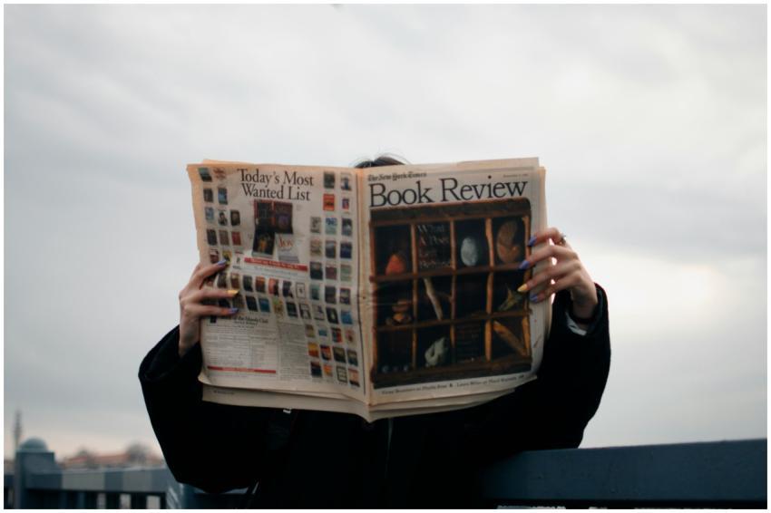 Individual holding a book review newspaper with co