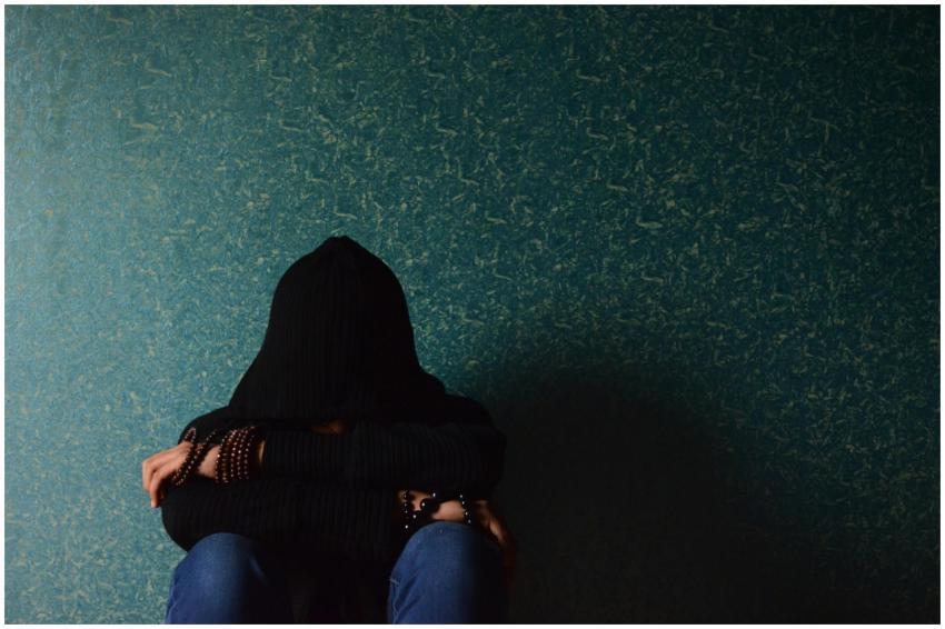 A person sits alone in a hoodie, conveying a sense