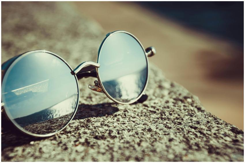 Round sunglasses resting on a sandy beach reflecti