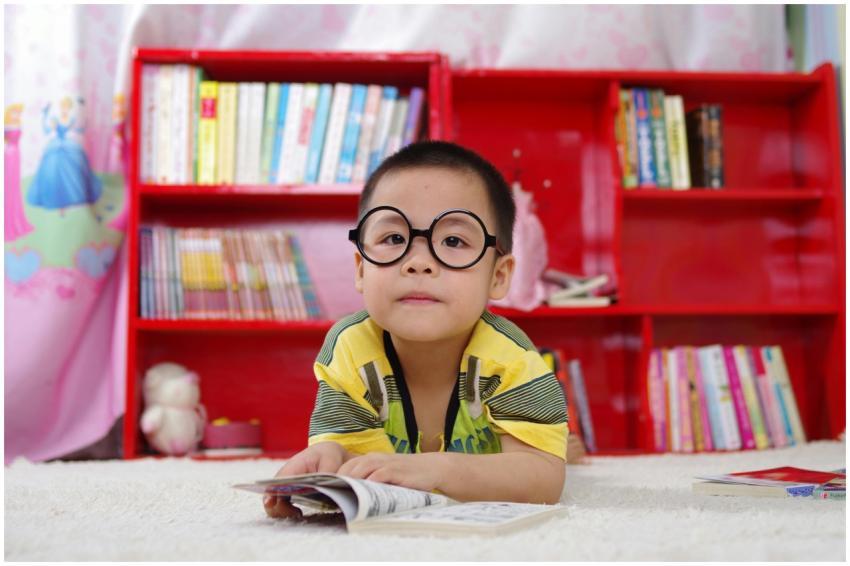 A cute child in glasses reading a book, surrounded