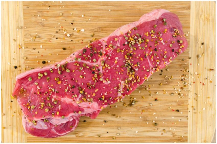 Close-up of a raw steak with spices on a wooden cu