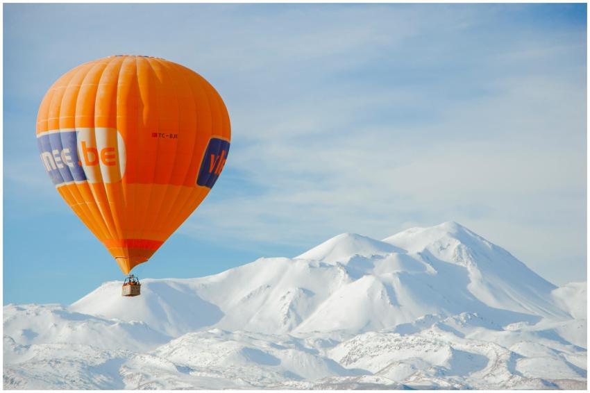 Orange hot air balloon flying over snow-covered mo