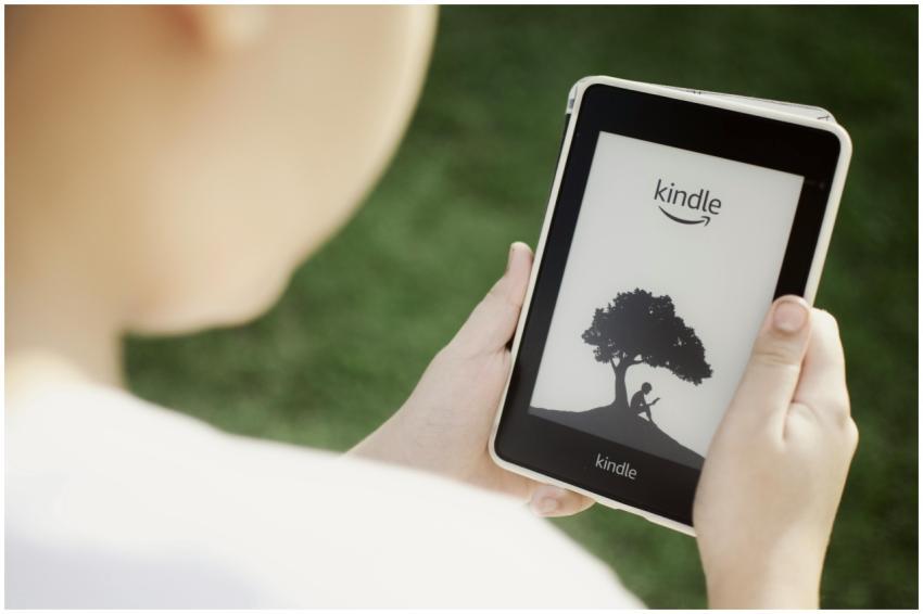 A child holds a Kindle device outdoors, highlighti