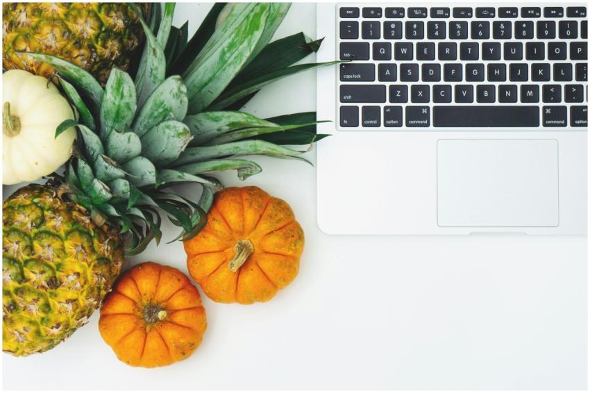A top view of pineapples, pumpkins, and a laptop o