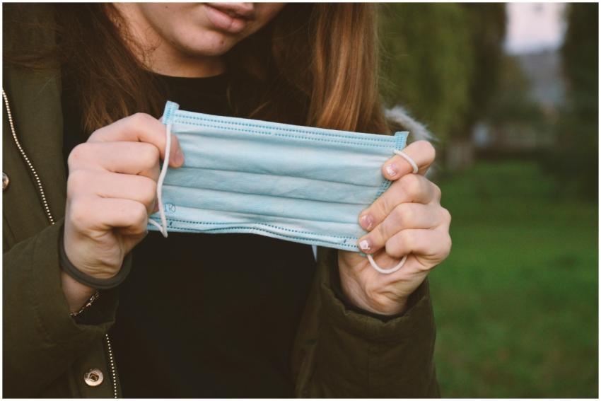 A woman outdoors holding a face mask, representing
