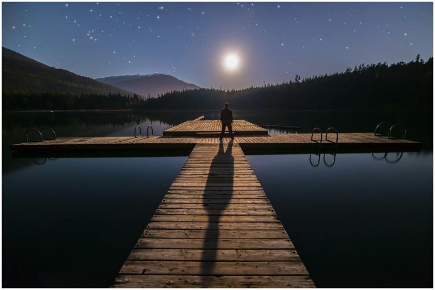 A man stands alone on a dock under a starry night