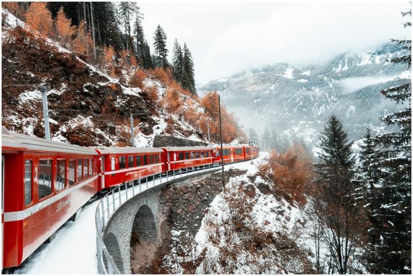 A red train navigates a snowy mountain landscape i