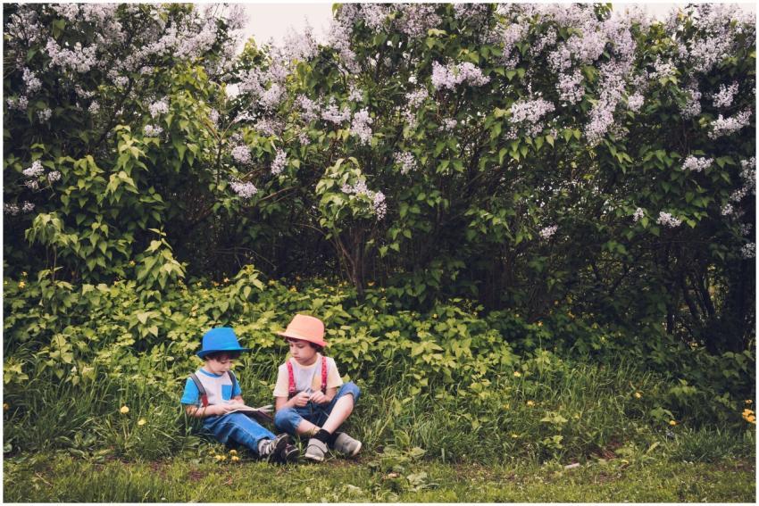 Two children sitting in a lush garden surrounded b