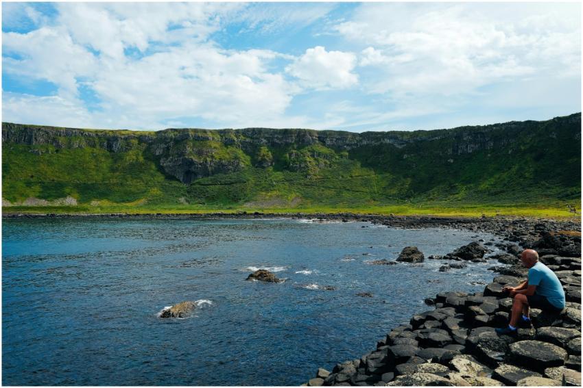 A man sits on the rocky coast of Giant's Causeway,