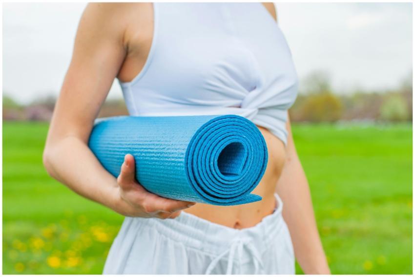 Close-up of a woman holding a blue yoga mat in a g