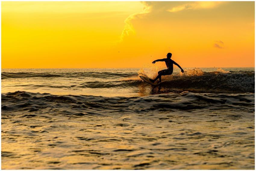 A silhouette of a surfer riding waves at sunset in