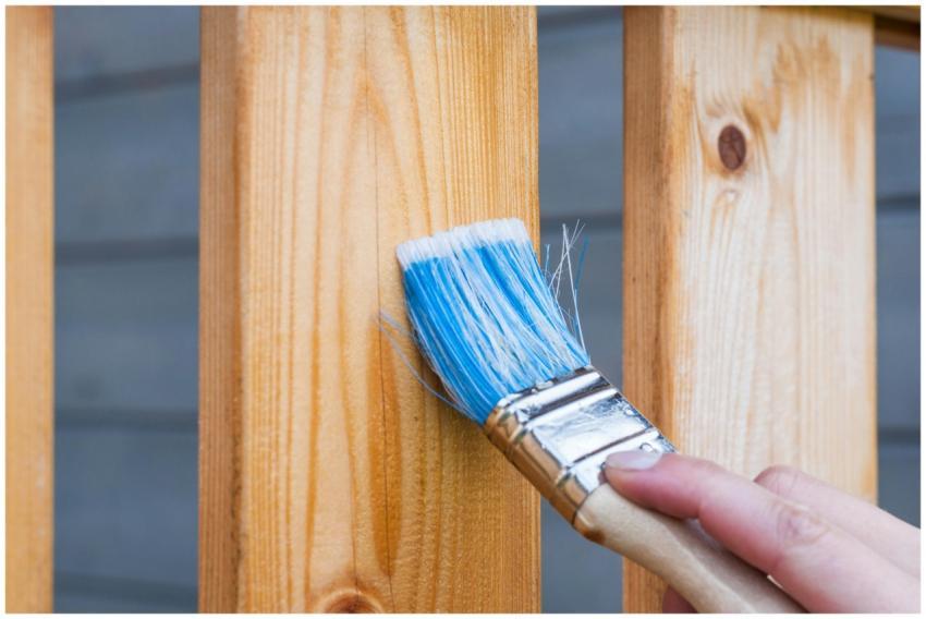 A hand painting a wooden fence plank with a blue p