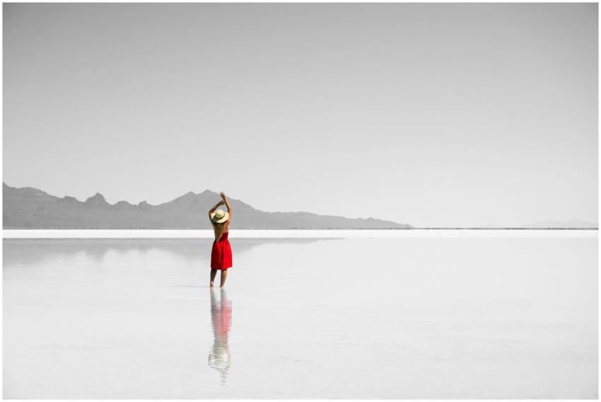 A woman stands in a reflective desert lake wearing