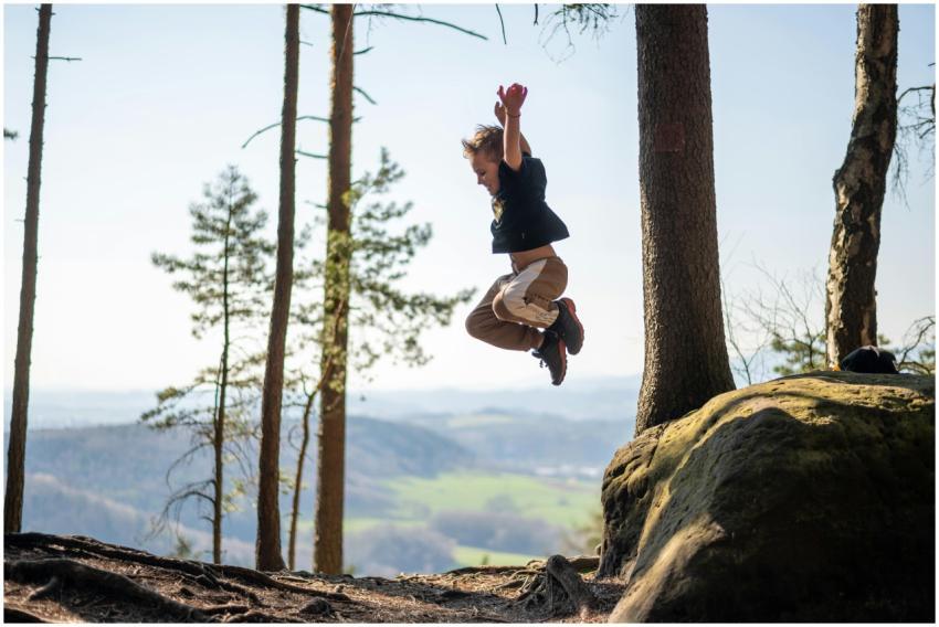 A young boy energetically jumps in a scenic forest