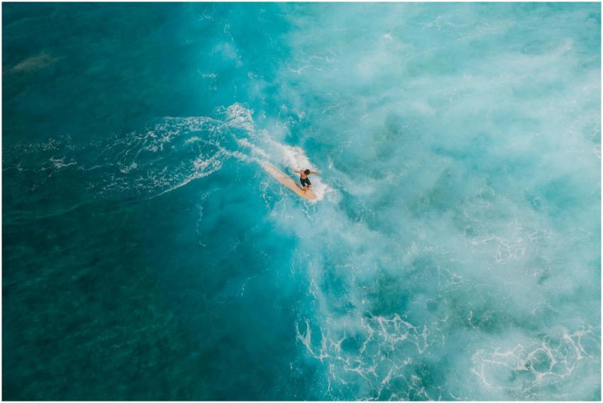 A lone surfer rides vibrant turquoise waves, viewe