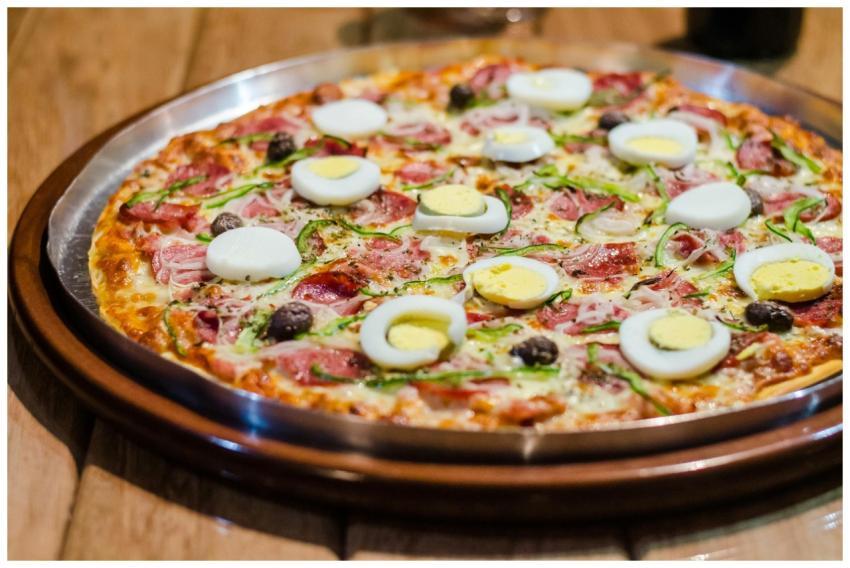 Close-up of a tasty pizza with eggs, ham, and oliv