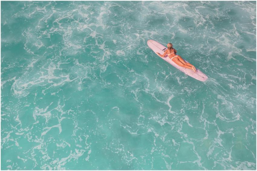 A woman surfer paddling on a surfboard in clear tu