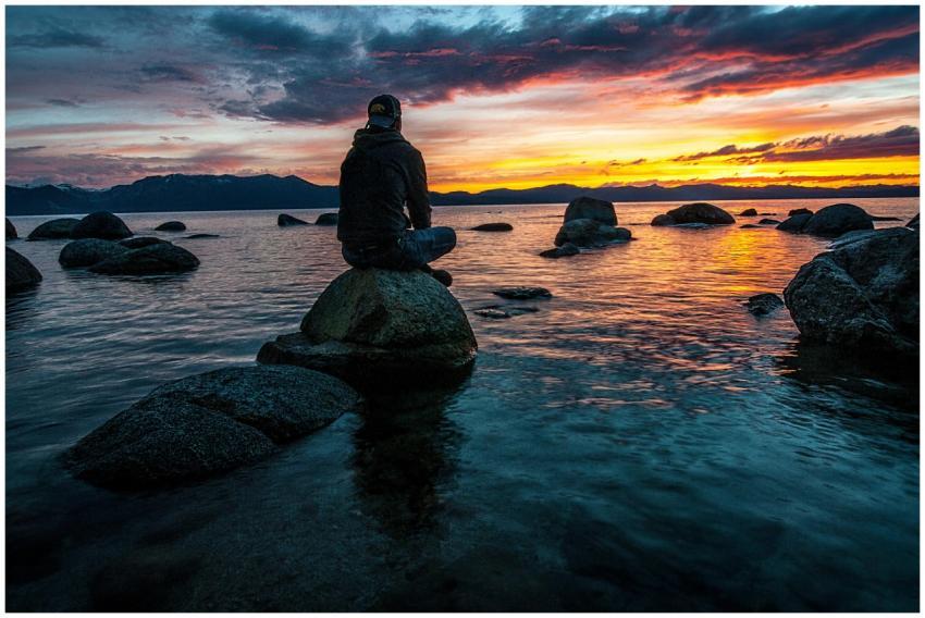 Silhouette of a man seated on rocks, gazing at a s