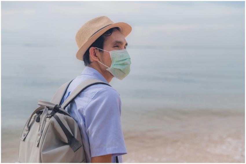 Man wearing a surgical mask and fedora backpacking