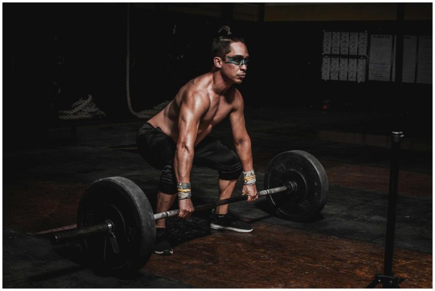 Strong athlete lifting heavy barbell in a dimly li