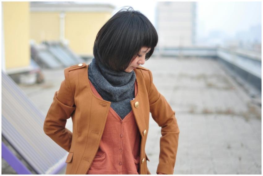 Woman in brown coat and scarf standing on rooftop