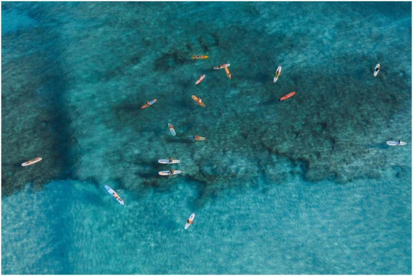 Surfers riding waves on clear blue waters from a h