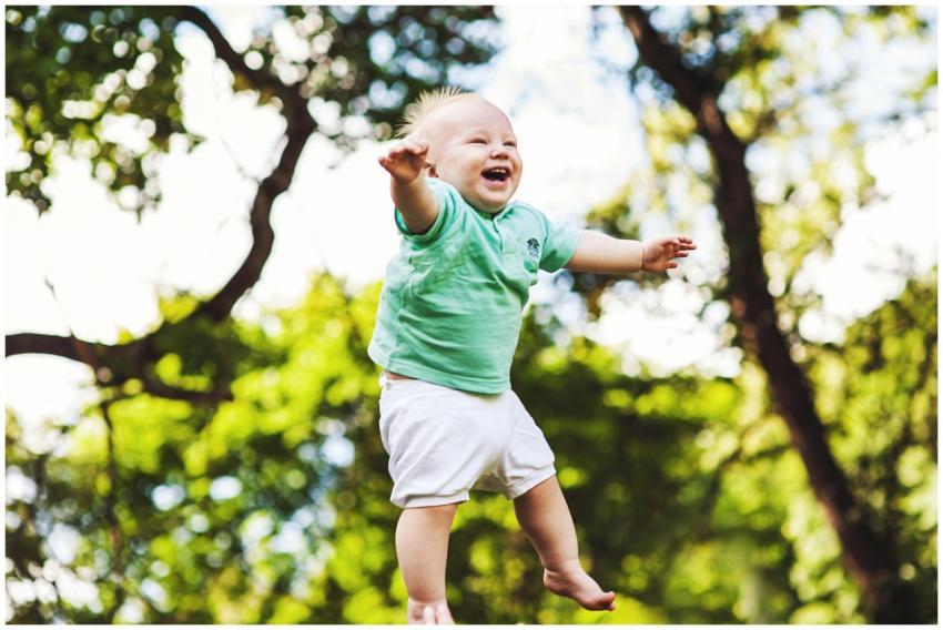 Happy baby wearing a green shirt being tossed in t