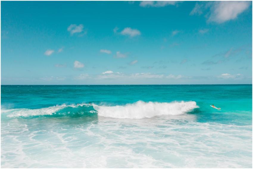 A surfer rides turquoise ocean waves under a clear
