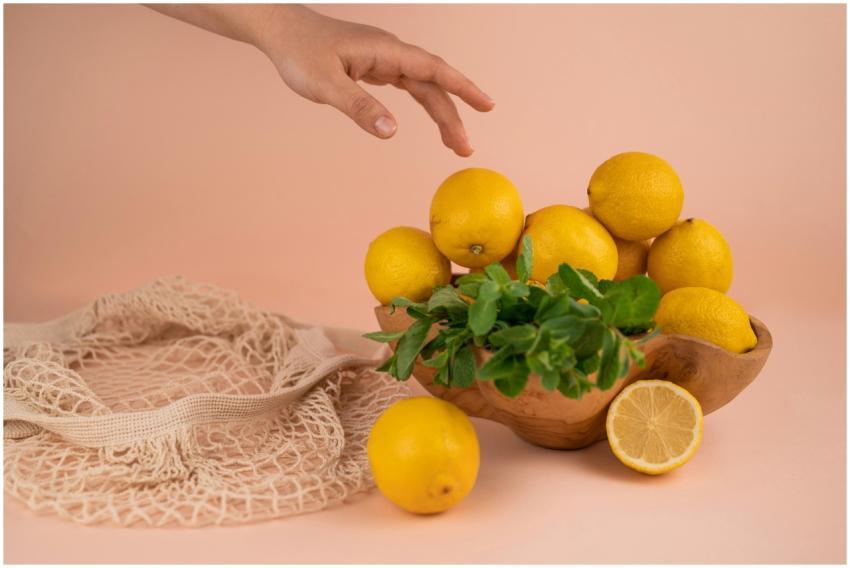 A hand reaching for fresh lemons in a wooden bowl