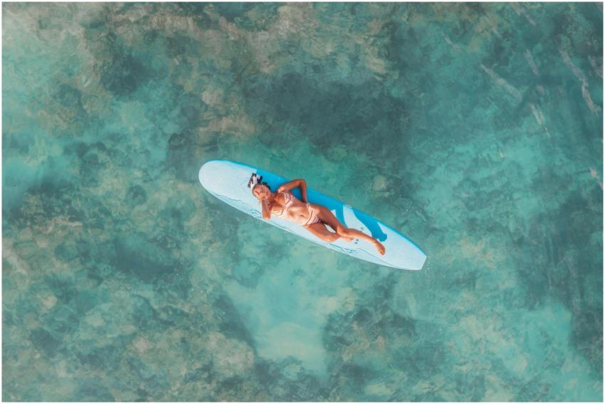 Aerial shot of woman lying on a surfboard in clear