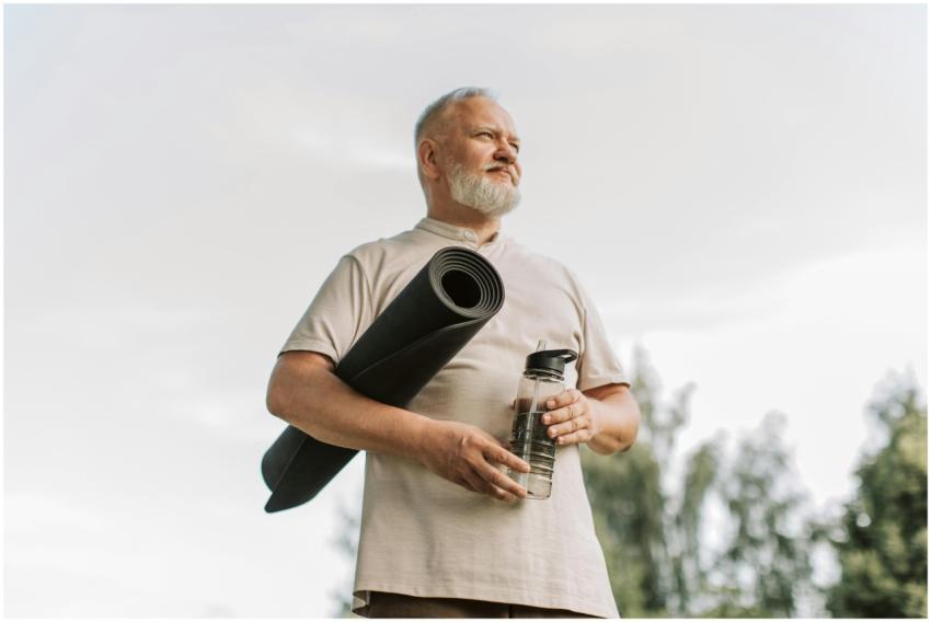 Elderly man with white hair holding a yoga mat and