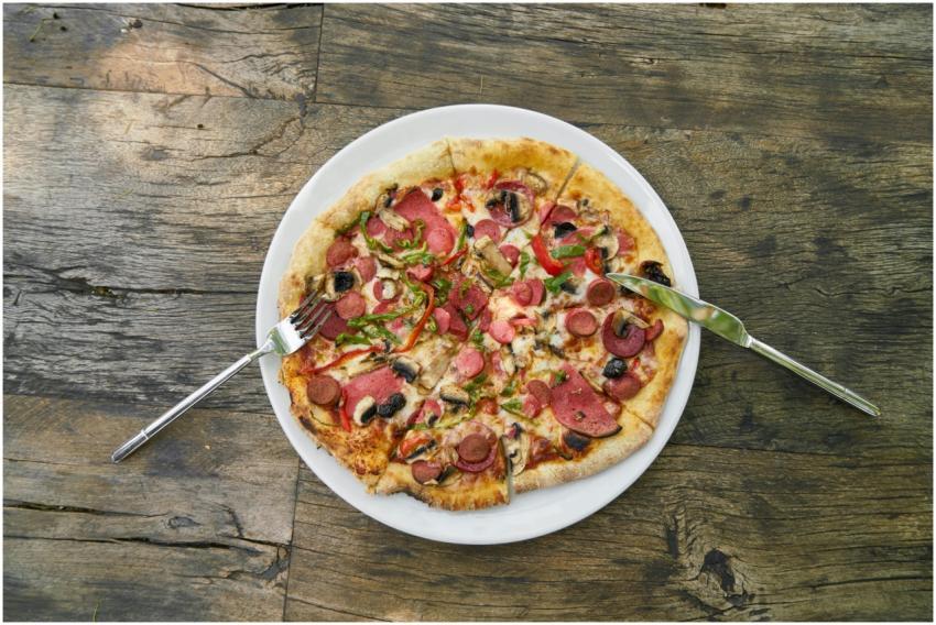 Top view of a pepperoni pizza with utensils on a r