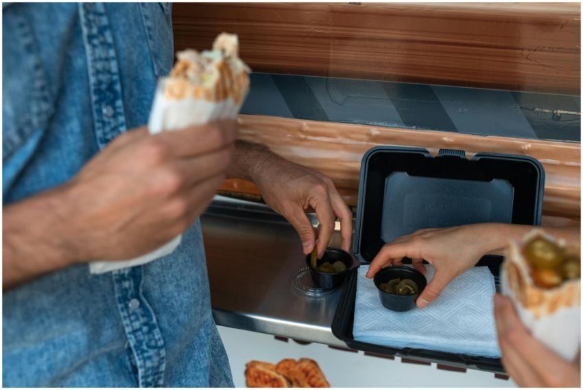 Hands holding shawarma and picking pickles at a fo