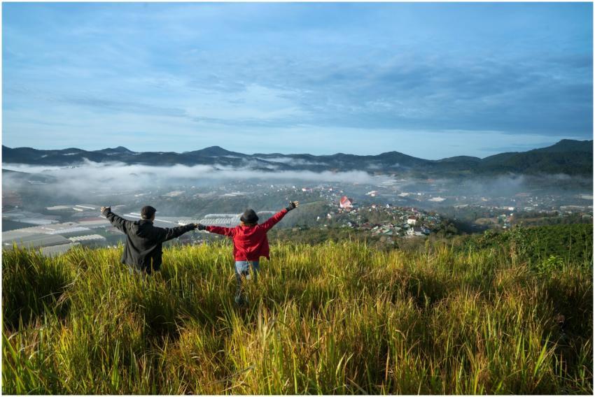 Couple standing on grassy hilltop overlooking a mi