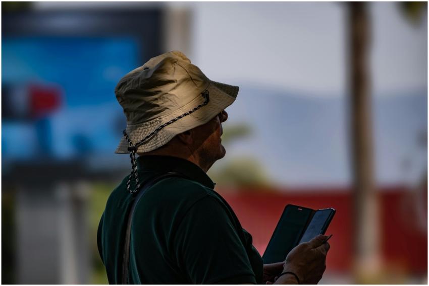 Man in silhouette wearing a hat, using a smartphon