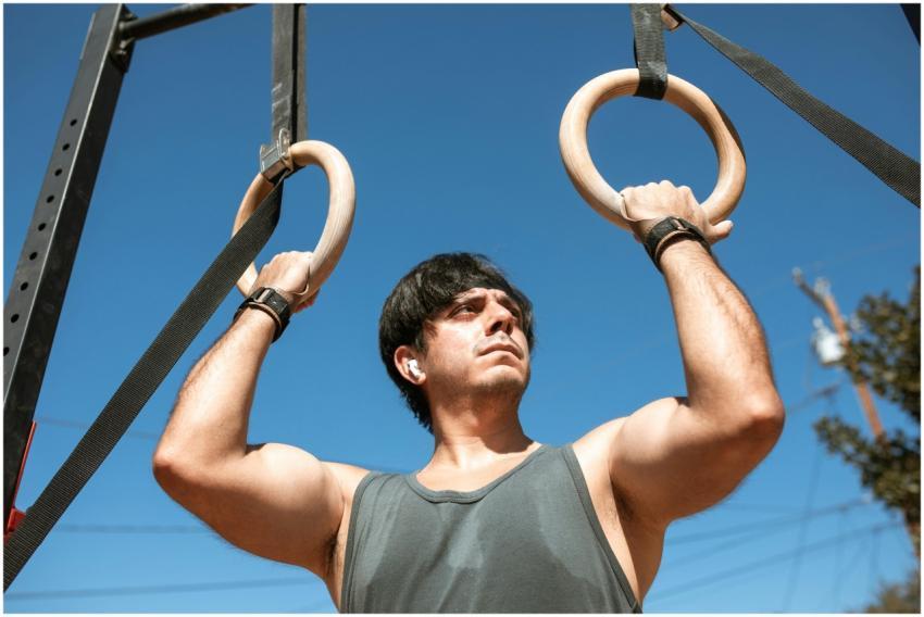 A man exercises with gymnastic rings outdoors, sho