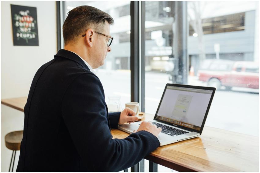 Adult male in cafe working on laptop, drinking cof