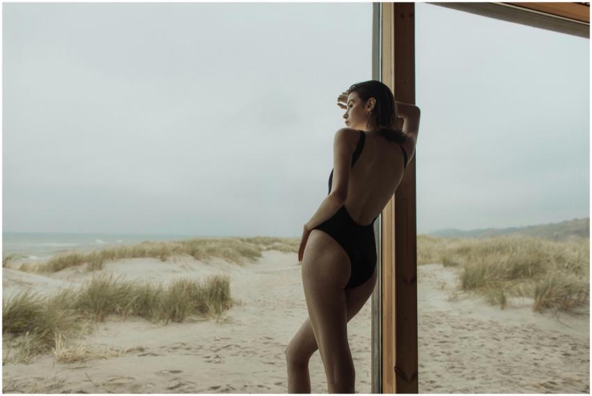 A woman in a backless swimsuit gazes out to the se