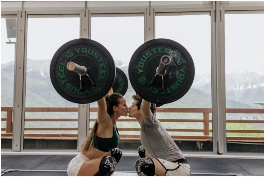 A couple in athletic gear kisses while lifting bar