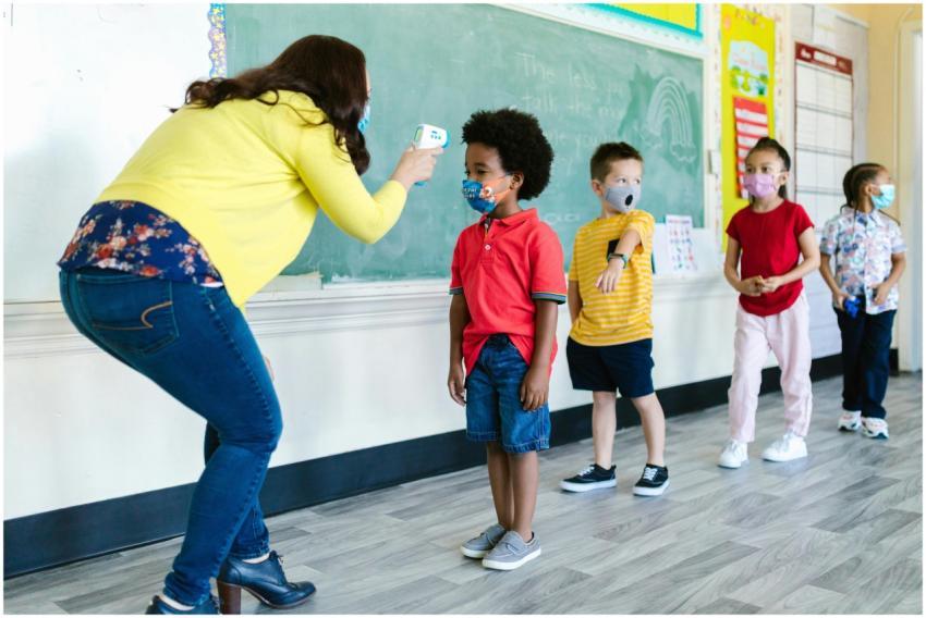 Teacher checking temperature of children in a clas