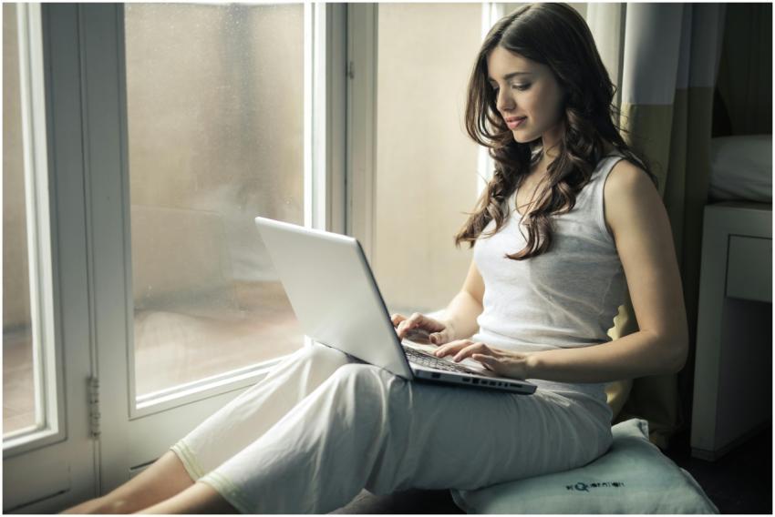 Adult woman sitting by window working remotely on