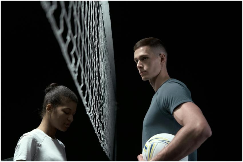 Two volleyball players face off across a net in a