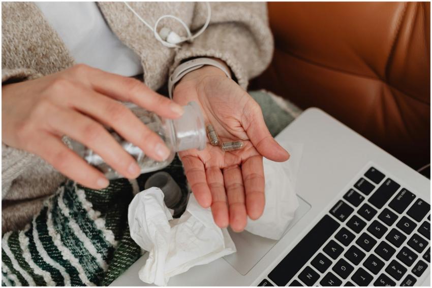 A person holding pills near a laptop, symbolizing