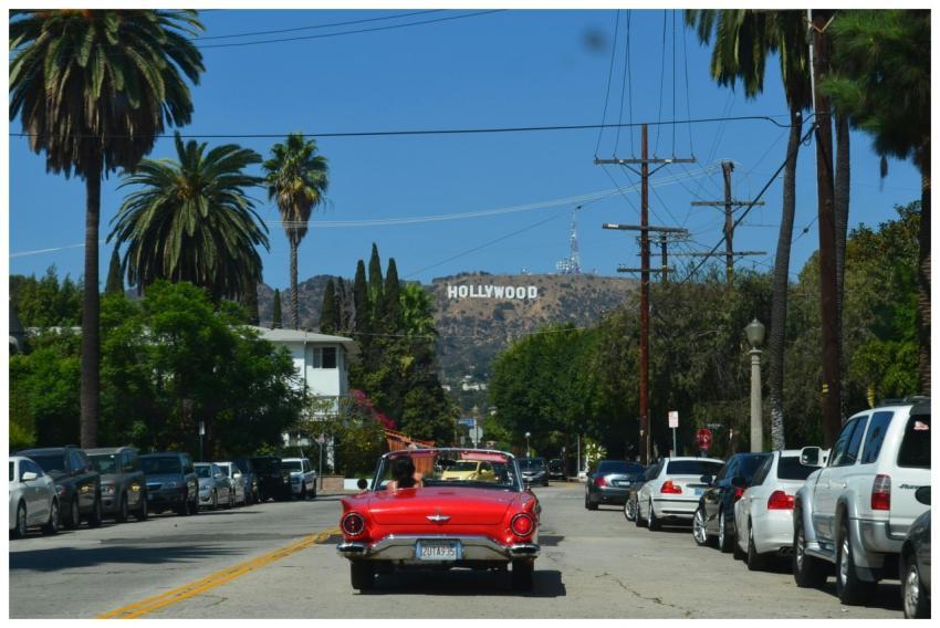 Red convertible driving down a sunny street toward